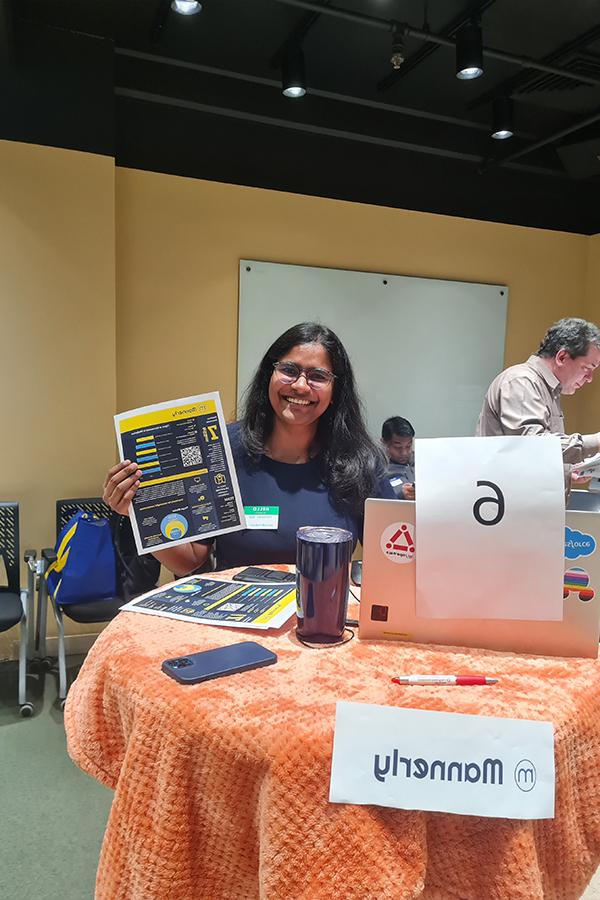 Pranathi stands at a circular table holding pamphlets about her startup, Mannerly