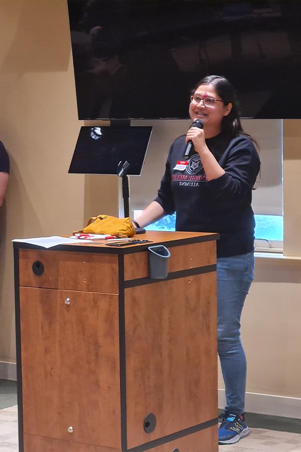 Shivani is standing at a podium holding a microphone while presenting her startup pitch